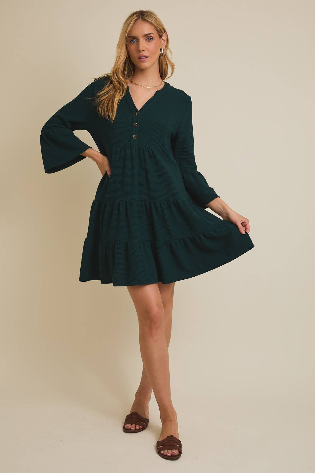 Woman wearing a dark green dress with bell sleeves on a beige background